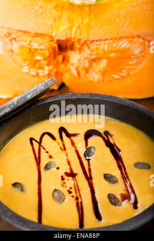 Kürbiscremesuppe mit Kernen und Kürbiskernöl in Speckstein pan, groß geschnittenen Kürbis im Hintergrund Stockfoto
