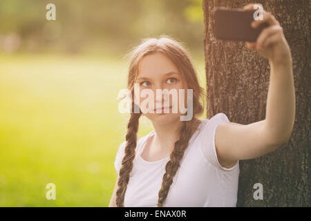 Teenager-Mädchen nehmen Selfie mit Handy im Park unter dem Baum Stockfoto