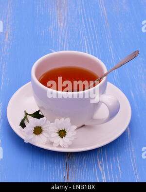 Weißer Teetasse und Blumen auf blauem hölzernen Hintergrund, vertikale Stockfoto