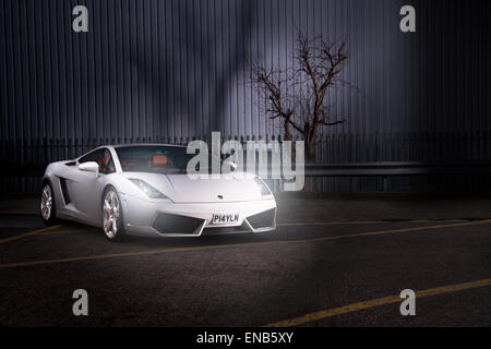 Lamborghini Gallardo in weiß setzte gegen industriellem Hintergrund. Vorderen 3/4 mit Scheinwerfern. Stockfoto
