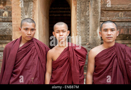 Porträt von einem drei buddhistische Mönche tragen rote Roben gegen die Steinmauer und Eingang zu einem Tempel in Bagan Myanmar Burma Stockfoto