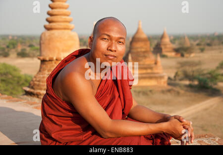 Porträt eines buddhistischen Mönchs sitting on Top of ein Tempel mit einer Linie der Tempel Türme im Hintergrund bei Sonnenuntergang Bagan Stockfoto