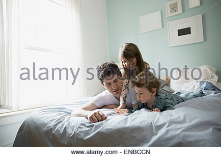 Vater und Kinder bei der Nutzung digitalen Tablets im Bett