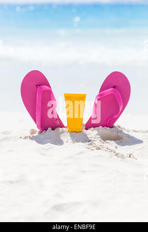 Rosa lebhaften Strand Flip-Flops mit Sonnencreme Schutz Gesichtscreme im weißen Sand am Meer-Hintergrund. Tropischer Sommer Urlaub con Stockfoto