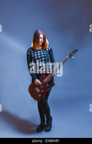 Europäische Erscheinung dunkelhaarige Mädchen in einem blauen Pullover, Gitarre zu spielen, auf einem grauen Hintergrund, Sehnsucht, Traurigkeit Stockfoto