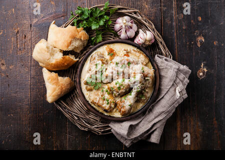 Gebratenes Huhn mit cremigen Knoblauchsoße in Ton pan Ketsi auf dunklem Holz Stockfoto