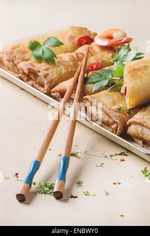 Frittierte Frühlingsrollen mit Gemüse und Garnelen, serviert mit pikanter Sauce und Stäbchen über weißen hölzernen Hintergrund. Stockfoto
