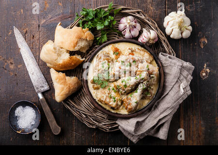 Gebratenes Huhn mit cremigen Knoblauchsoße in Ton pan Ketsi auf dunklem Holz Stockfoto