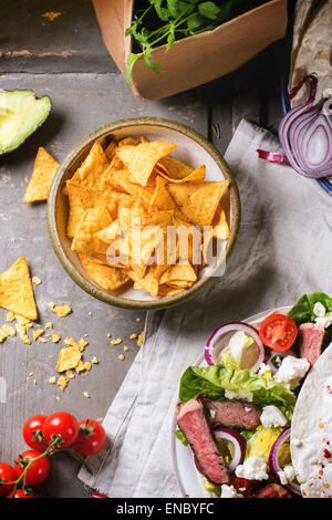 Draufsicht auf mexikanischen Stil Abendessen mit Gemüse, Tacos, Nachos Chips und Guakomole, serviert auf grauem Holztisch. Stockfoto