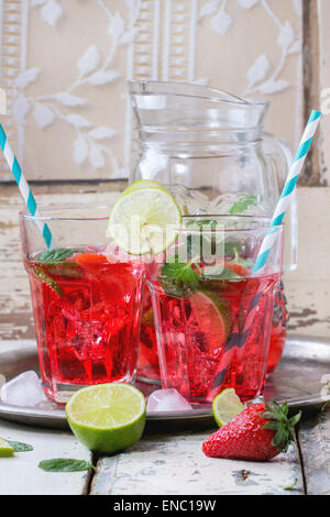 Zwei Gläser mit Retro-cocktail Röhren und Glaskrug mit hausgemachtem Erdbeer Limonade, serviert mit frischen Erdbeeren, Minze, Limette Stockfoto