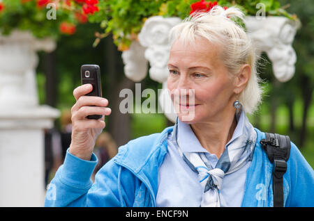 eine Frau mittleren Alters fotografiert in einem Park am Telefon Stockfoto