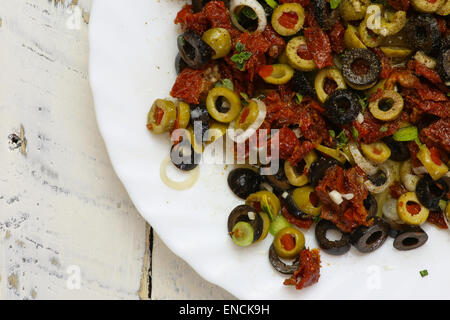 In Scheiben geschnittenen grünen und schwarzen Oliven, getrockneten Tomaten, Oregano Blätter und junge grüne Knoblauch auf weißen Teller, weißen Teig Hintergrund, Stockfoto