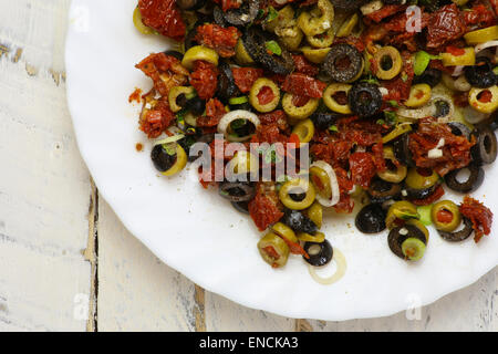 In Scheiben geschnittenen grünen und schwarzen Oliven, getrockneten Tomaten, Oregano Blätter und junge grüne Knoblauch auf weißen Teller, weißen Teig Hintergrund, Stockfoto