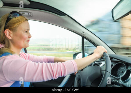 Attraktive Erwachsene Frau sicher und vorsichtig fahren Auto s unterwegs. Innen Auto Foto mit hoher Geschwindigkeit entgegenkommenden LKW truck Stockfoto