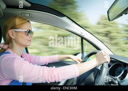 Hübsche Frau mit Sonnenbrille fahren schnelle Autos mit Panorama-Windschutzscheibe. Slow-Shutter bei hoher Geschwindigkeit in Bewegung Hintergrund verschwommen. Stockfoto