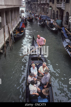 Venedig, Provinz Venedig, Italien. 1. September, 1985. In einer klassischen Gondel gestreiftes trägt ein traditionelles Hemd, ein Gondoliere Polen eine Touristengruppe in einen belebten kleinen Kanal. Venedig, ein UNESCO-Weltkulturerbe zählt zu den beliebtesten internationalen Reisezielen. © Arnold Drapkin/ZUMA Draht/Alamy Live-Nachrichten Stockfoto