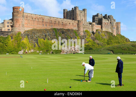 Drei Männer spielen Krocket auf dem Dorfplatz vor Bamburgh Castle, Bamburgh, Northumberland, England, UK Stockfoto