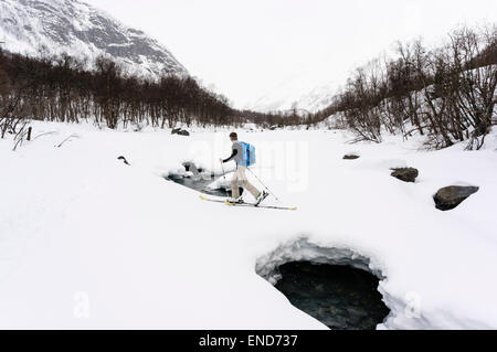 Ein Skifahrer Skitouren entlang eines Flusses im Schnee auf dem Weg nach oben Daltinden, Lyngen Alpen (Lyngsalpene), Troms, Norwegen. Stockfoto