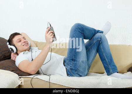 Junger Mann lächelnd genießen Musik mit Kopfhörer und Handy, Guy entspannend auf Couch zu Hause anhören von Musik über Handy Stockfoto