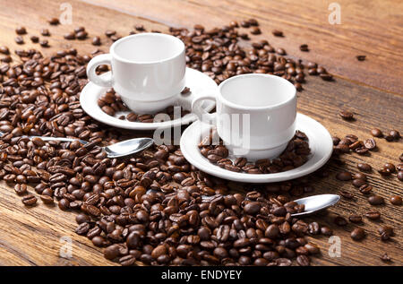 Zwei leere Kaffeetassen und Löffel unter Kaffeebohnen auf einem Holztisch. Stockfoto