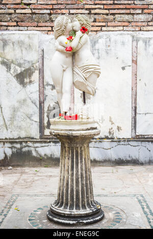 Die Statue von Amor und Psyche befindet sich in Ostia Altstadt, Rom, Italien. Natürliches Licht, rote Blüten. Stockfoto