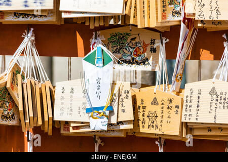 Holztafeln, Ema-Bretter, Votivtafeln, mit Reizen, die an Metallhaken auf einem verzinslichen bemalten Brett an einem schintoistischen Schrein in Japan hängen. Stockfoto