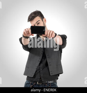 Junge bärtige Mann unter Foto mit seinem Smartphone-Kamera. Entsättigt über Retro-Vignette-Studio-Hintergrund Stockfoto