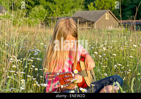 Junges Mädchen Gitarre auf einem ländlichen Gebiet von wilden Gänseblümchen. Stockfoto