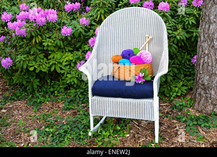 Bright farbigen Garn in einem Korb auf weißen geflochtenen Schaukelstuhl in einem Rhododendron-Garten. Stockfoto