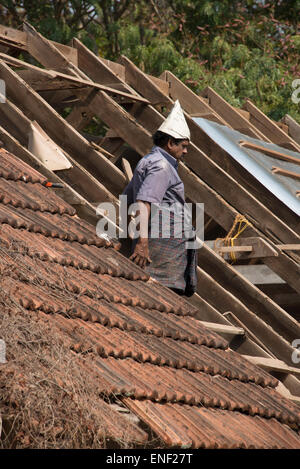 Ein Dachzieher, der einen handgefertigten Papierhut auf einem Dach eines alten Gebäudes in Fort Cochin, Kochi, Kerala, Indien trägt. Stockfoto