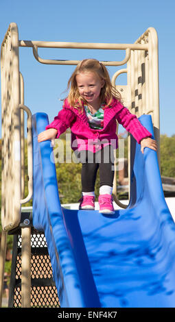 Kleines Mädchen auf einer blauen Folie auf einem Spielplatz spielen Stockfoto