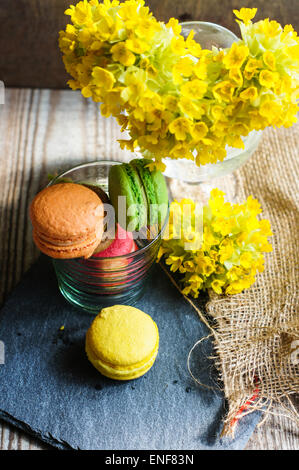 Bunte Makronen und ersten Frühlingsblumen auf alten hölzernen Hintergrund Stockfoto