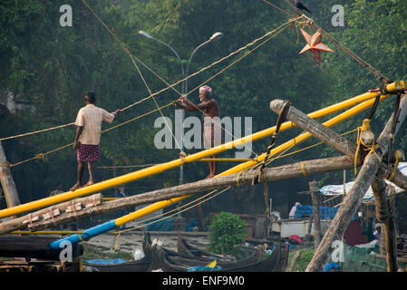 Ein paar Fischernetzbetreiber auf einem der chinesischen Fischernetze in Fort Cochin, Kochi, Kerala, Indien werden die Netze abgesenkt ar Stockfoto