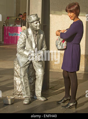 Mann als Straßenmusikant als lebende Statue mit Silber Körper, Kleidung und Hut, die Interaktion mit lächelnden Asiatin am Circular Quay in Sydney Australia Stockfoto