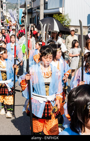 Ein Team von Kindern, Mädchen, die als Shimobe-Soldaten der Heian-Ära verkleidet in der Frühlingsparade von Genji durch die Stadtstraße in Tada, Japan marschieren. Stockfoto