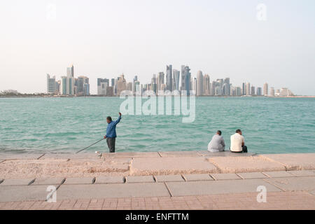 Drei asiatische Männer vergehende Zeit an der Uferpromenade Corniche in Doha, Katar, mit der Skyline der Stadt im Hintergrund zu sehen. Stockfoto