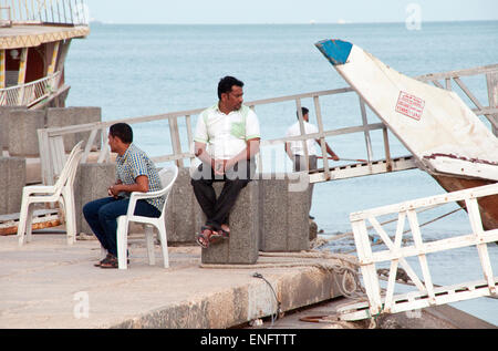 Touristischen Dhow Boot Arbeiter sitzen am Wasser durch ihre festgemachten Schiffe warten auf Passagiere, in Doha, Katar. Stockfoto