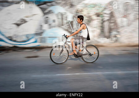 Havanna, Kuba - 18. Mai 2011: Junger kubanische Mann reitet sein Fahrrad hinter einer Wand von Graffiti auf einer Straße in Zentral-Havanna. Stockfoto