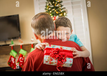 Kaukasische Enkel umarmt Großvater mit Weihnachtsgeschenk Stockfoto