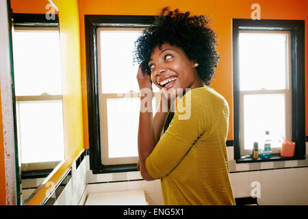 Schwarze Frau Haar-Styling im Badezimmerspiegel lächelnd