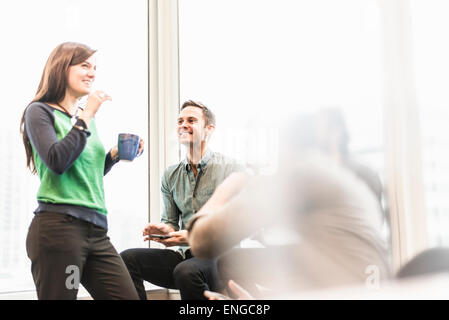 Ein Mann und eine Frau mit einer Tasse Kaffee in einem Büro zu sprechen. Stockfoto