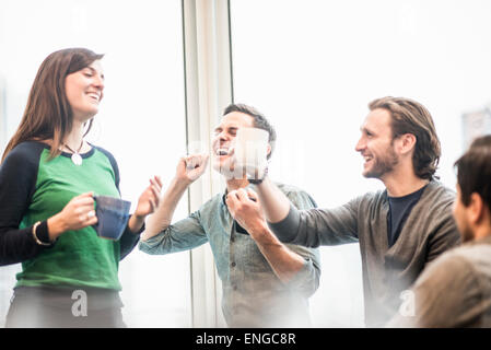 Vier arbeiten Kolleginnen und Kollegen auf eine Pause, lachen und erhöhen ihre Kaffeetassen. Stockfoto