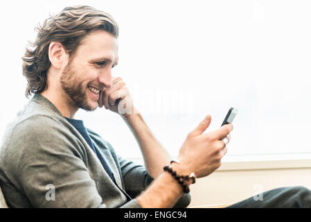 Ein bärtiger Mann sitzt lächelnd und überprüft seine Telefon. Stockfoto