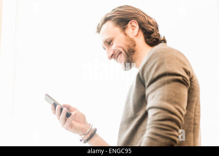 Ein bärtiger Mann lächelnd und überprüft seine Telefon. Stockfoto