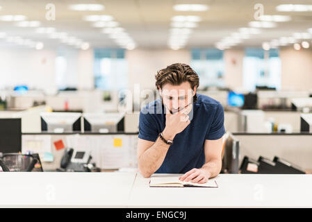 Ein Mann stützte sich auf seine Ellbogen und mit Blick auf ein offenes Buch auf einem Schreibtisch. Stockfoto