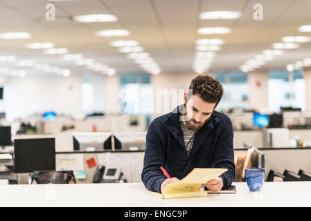 Ein Mann sitzt an einem Schreibtisch in einem Büro mit einem roten Stift schreiben. Stockfoto