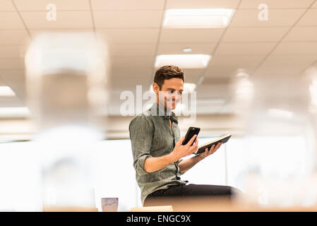 Ein junger Mann sitzt auf seinem Smartphone hält ein offenes Notebook. Stockfoto