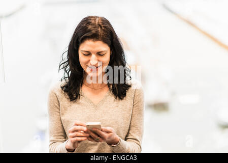 Eine Business-Frau sitzt an einem Fenster mit ihrem Smartphone. Stockfoto