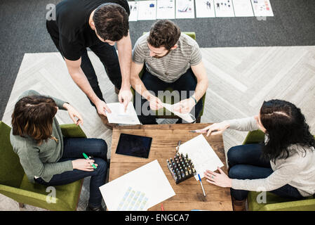 Vier Personen sitzen an einem Tisch mit Farbstiften auf Papier, Kollegen bei einem Vorgespräch. Stockfoto