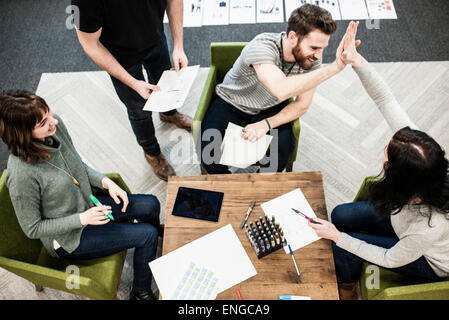 Vier Personen sitzen an einem Tisch, Kollegen bei einer Planung treffen hohe Fiveing einander. Stockfoto